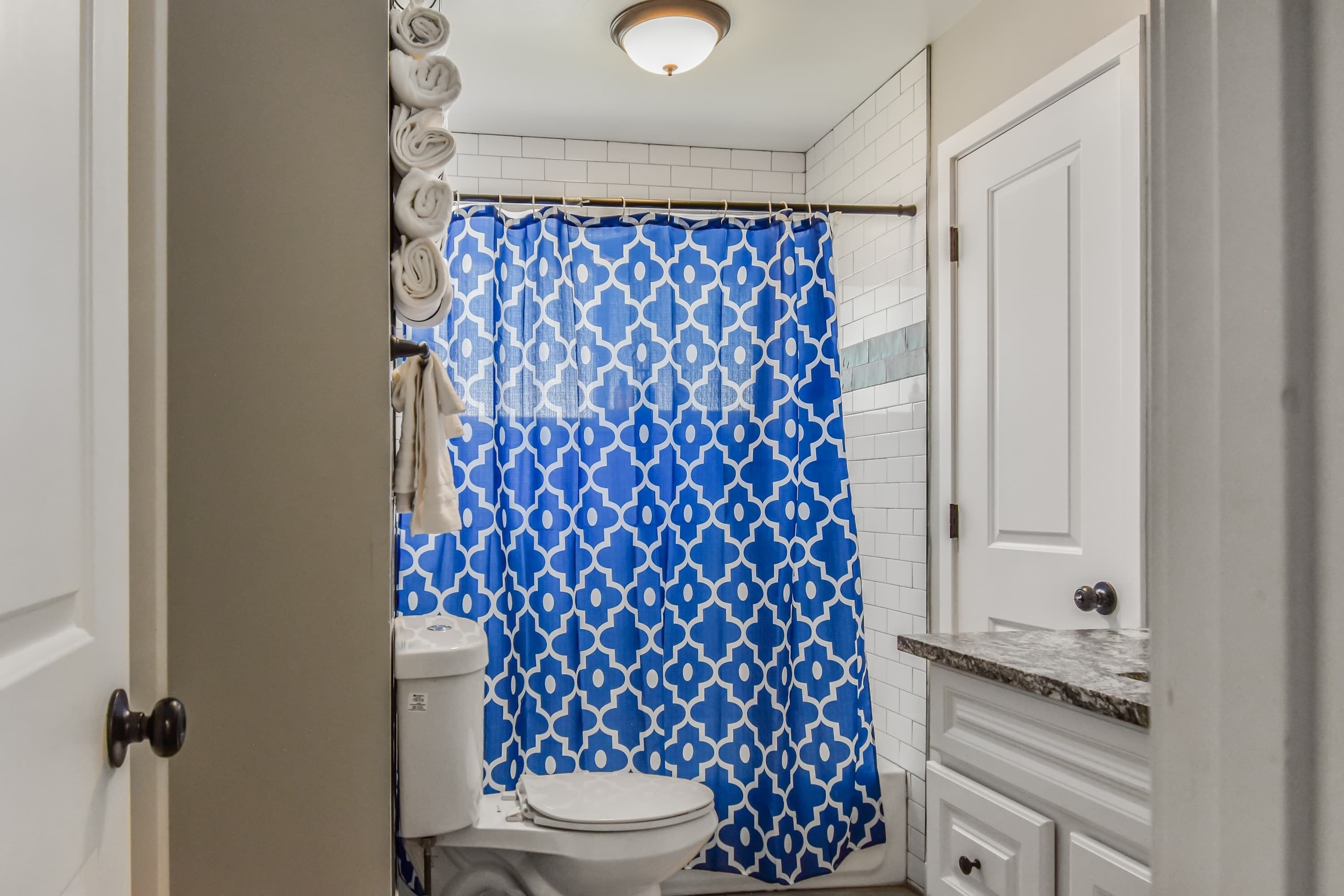 A bathroom with a white toilet, a blue patterned shower curtain, and a white tiled wall.