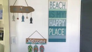 Uma parede com placas decorativas, incluindo uma com a frase 'The Beach is my happy place'.