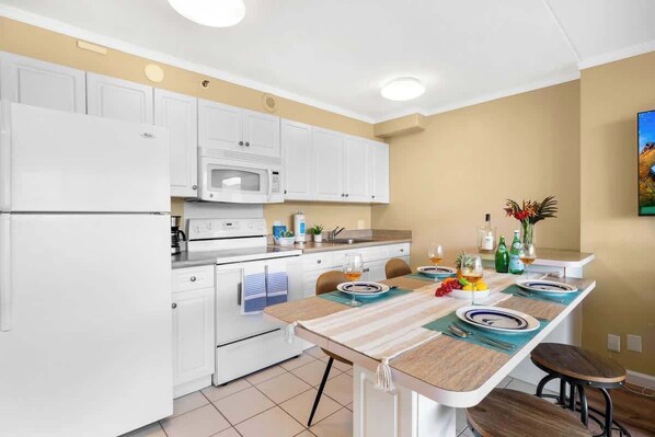 Una cocina moderna con armarios blancos, un microondas y un comedor para cuatro personas, con una mesa, sillas y un taburete de bar.