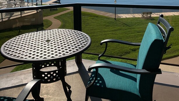 Un balcón con una mesa y sillas que da a un lago, un muelle y una zona verde.