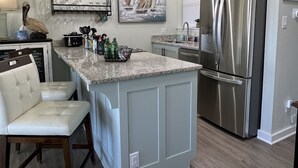 Una cocina moderna con una isla central, electrodomésticos de acero inoxidable, iluminación colgante y un cuadro de un velero en la pared.