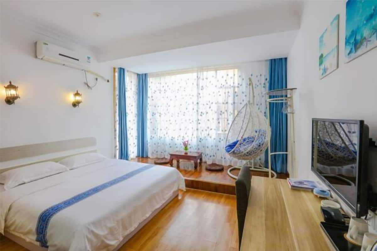 Une chambre à coucher comprenant un lit, un bureau, une chaise, un fauteuil suspendu, une télévision et une fenêtre avec des rideaux.