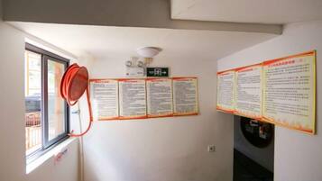 Ein Zimmer mit Fenster, Deckenventilator und mehreren Informationspostern an der Wand.