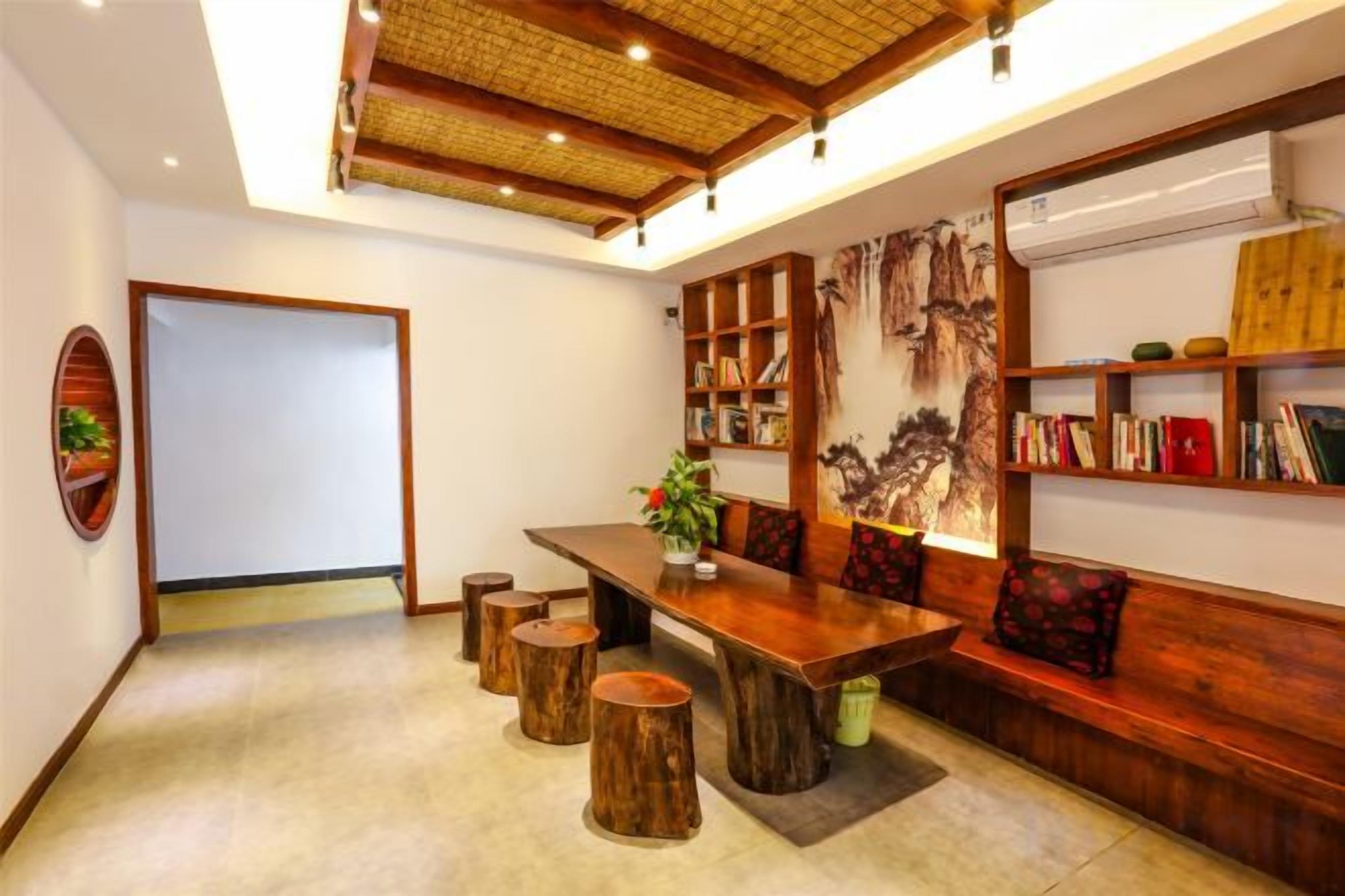 A room with a wooden dining table, stools, a bookshelf, and a wall-mounted air conditioning unit.