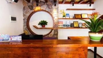 Een receptiebalie met een houten blad, een stenen muur, een ronde spiegel en een plank met omlijste decoraties en een potplant.