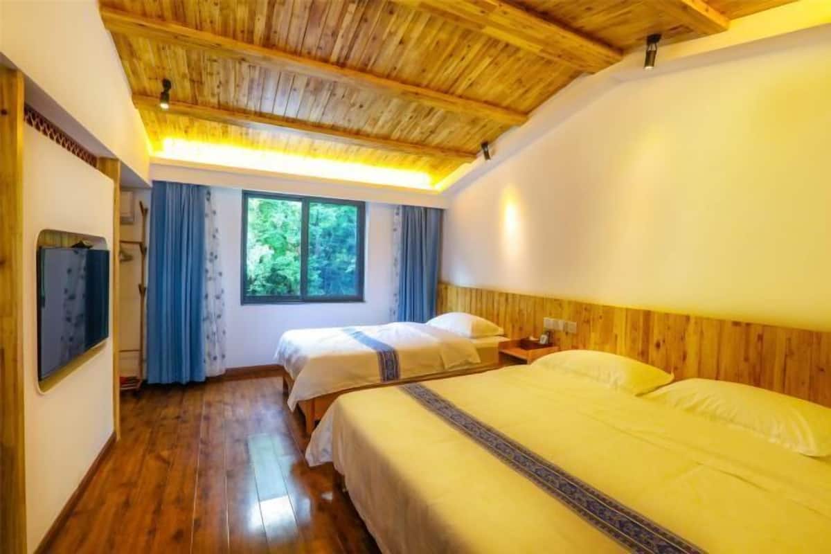 Une chambre avec un plafond en bois, deux lits, une télévision et une fenêtre avec des rideaux.