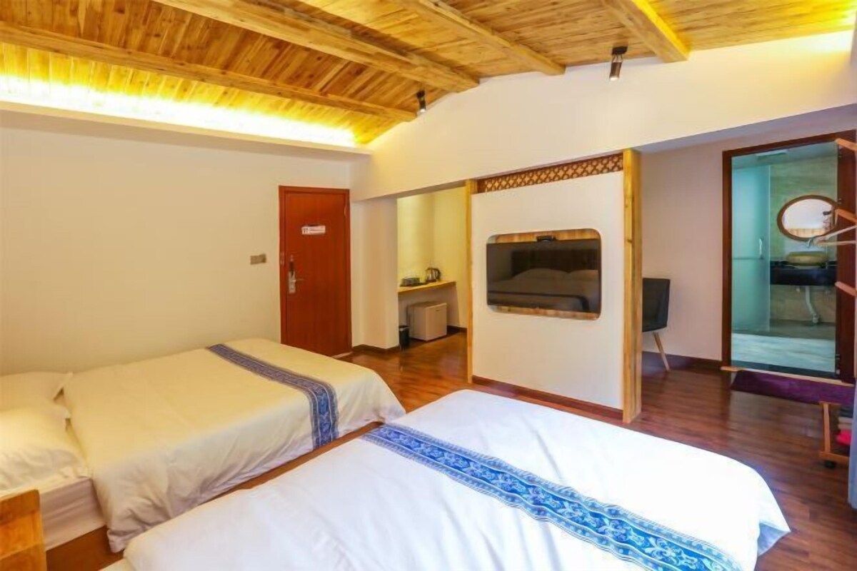 Una habitación con dos camas, techo de madera, televisor y una puerta que da a otra habitación.