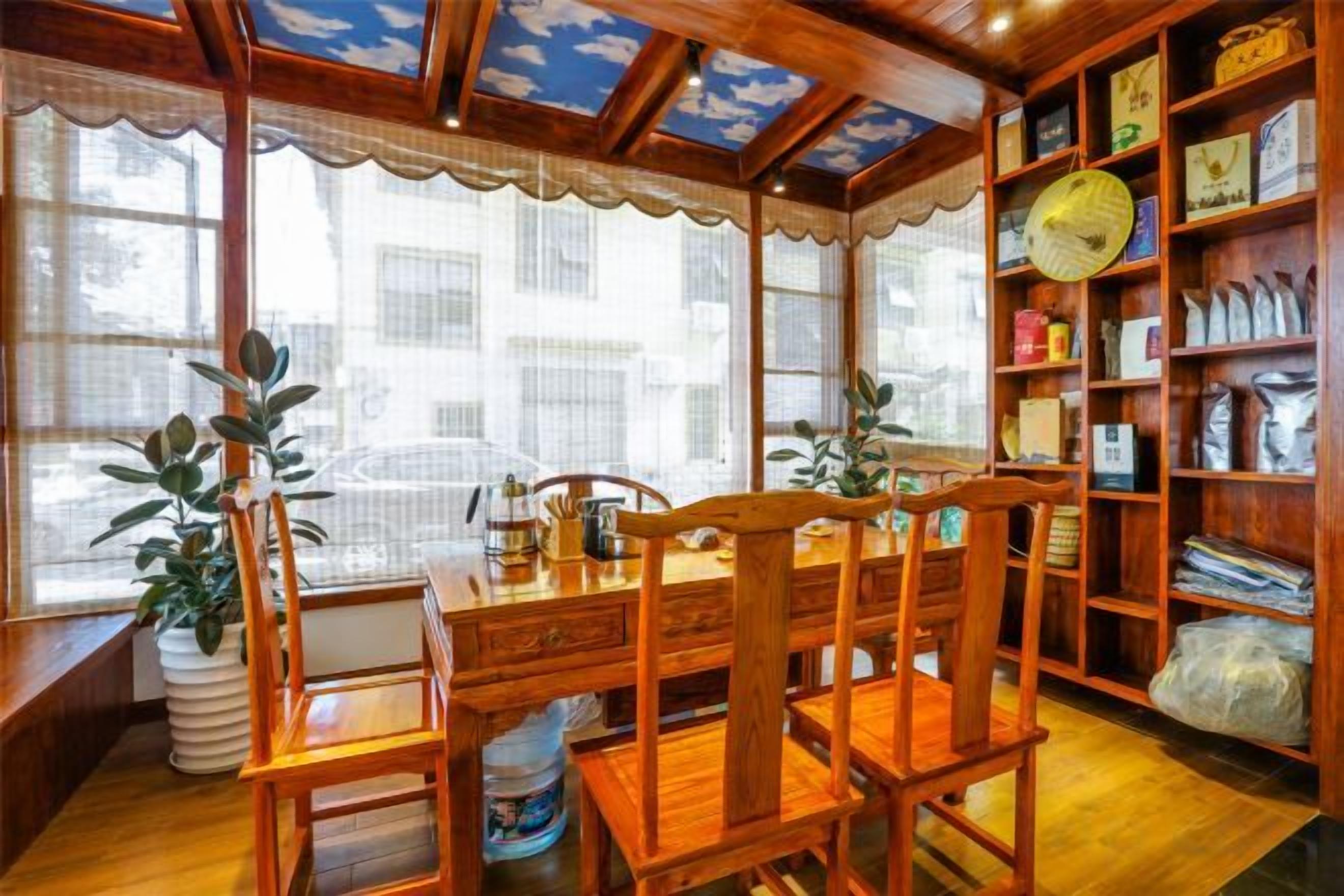 A room with a wooden dining table, chairs, a bookshelf, and a window with a view of buildings.