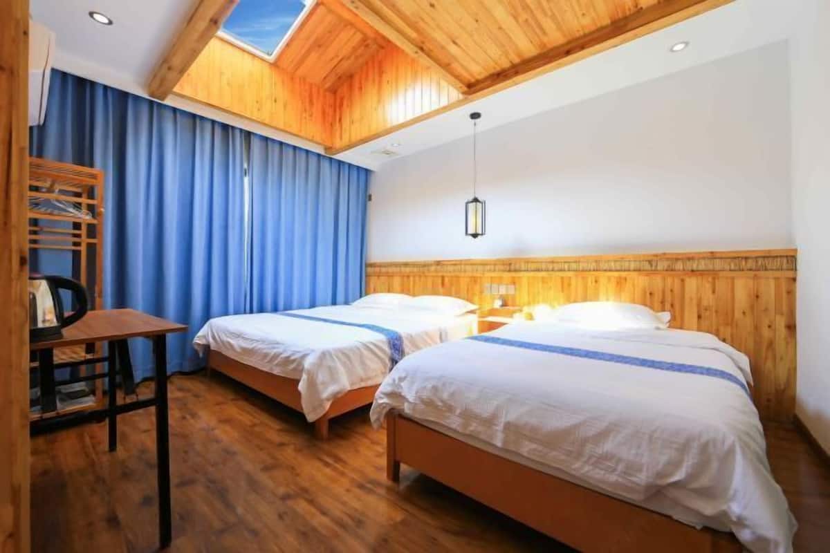 Une chambre avec deux lits, un plancher en bois, un bureau et une lucarne.