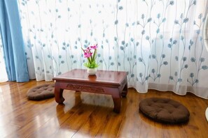 A wooden table with a vase of flowers, two pet beds, and a floral curtain in a room with wooden flooring. - Shanhai Coffee Inn (Zhangjiajie)