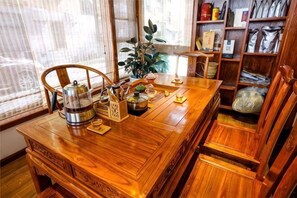 Una mesa de comedor de madera con sillas, una cafetera, una planta en maceta y una estantería con varios objetos.