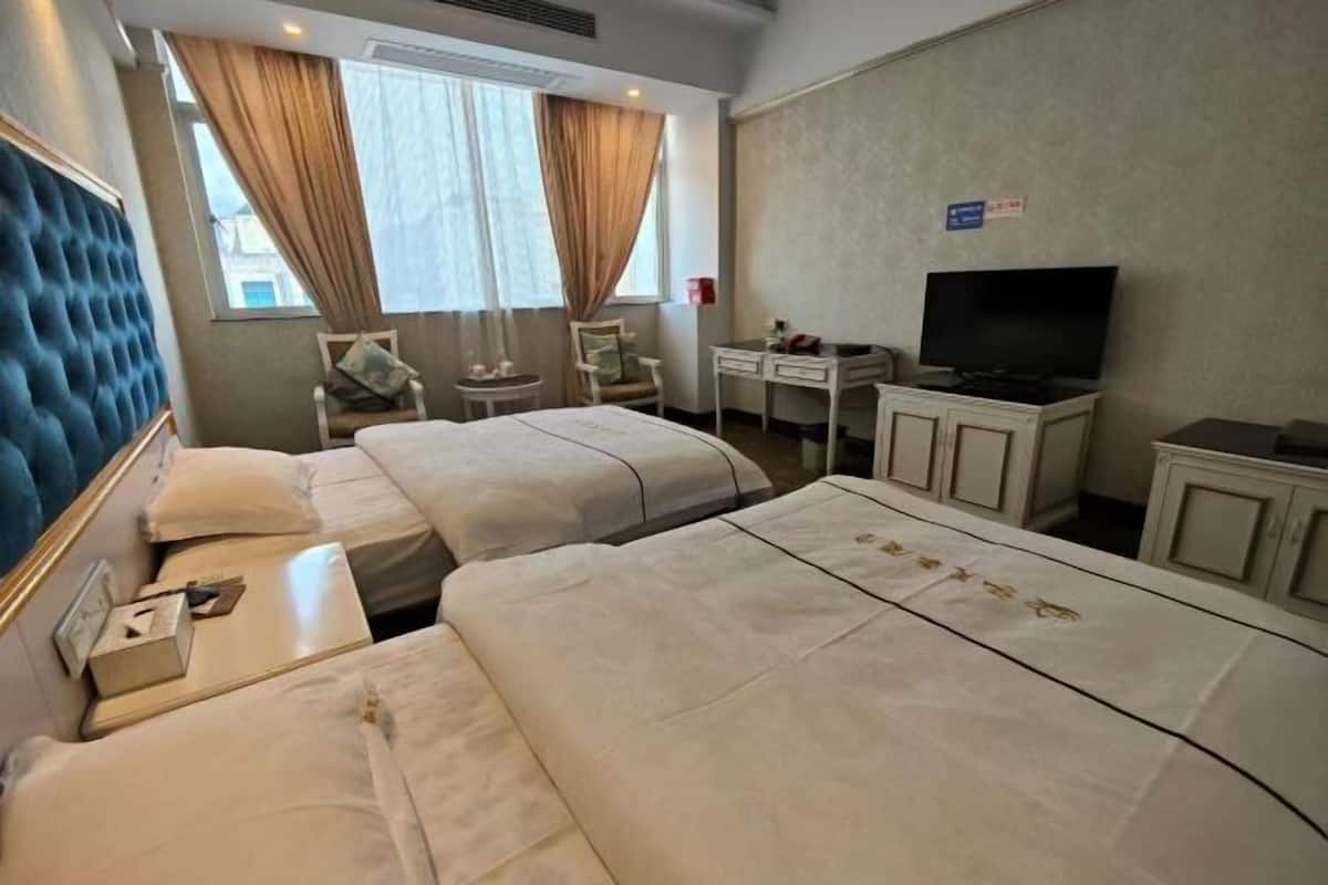 Ein Hotelzimmer mit zwei Betten, einem Schreibtisch, einem Stuhl, einem Fernseher und einem fenster mit Vorhängen.