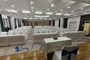 A conference room with rows of white tables and chairs, a carpeted floor, and a ceiling with recessed lighting. - Hongfurong Hotel (Anlong)