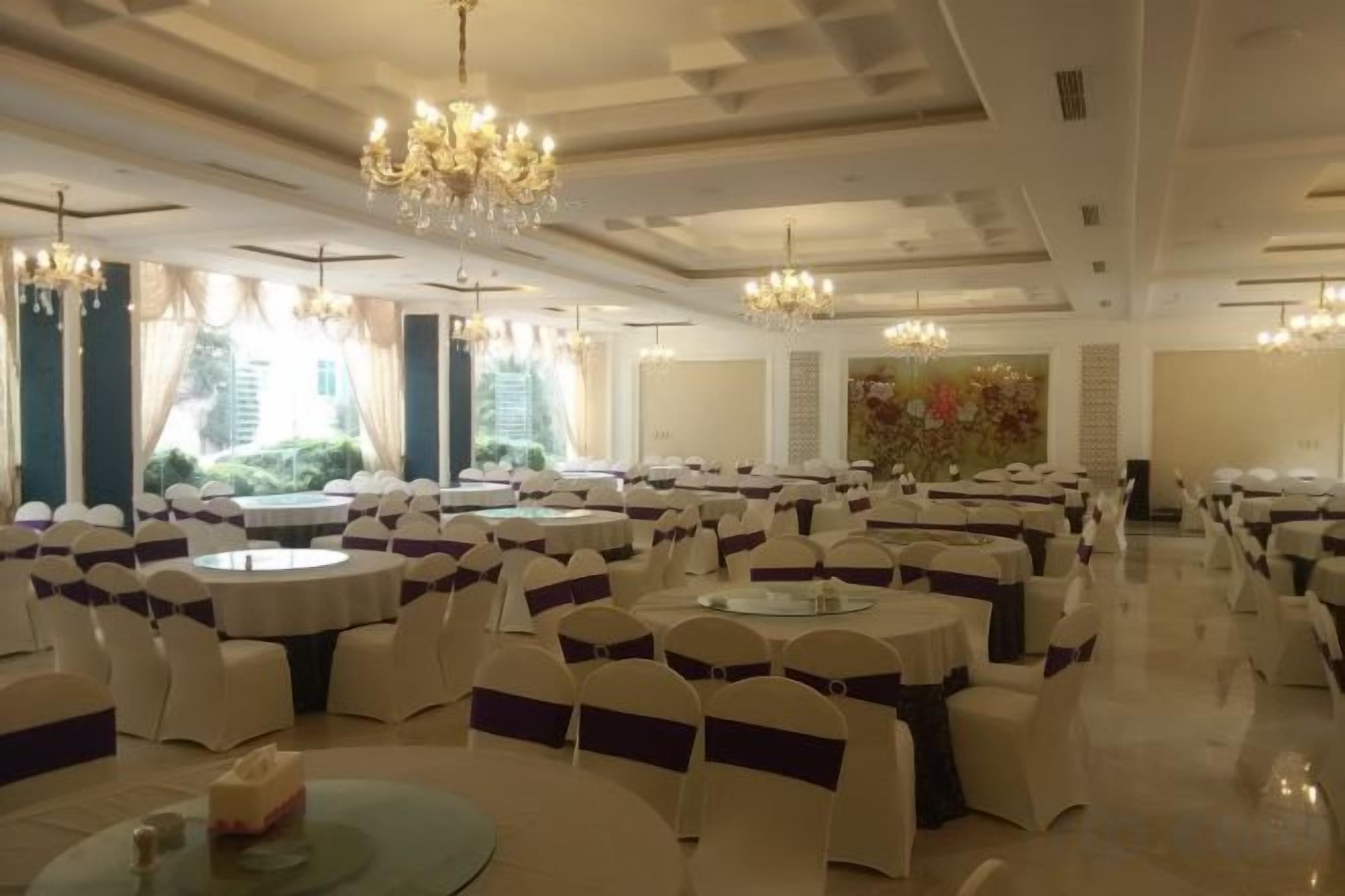 A banquet hall with round tables and chairs, chandeliers, and large windows.