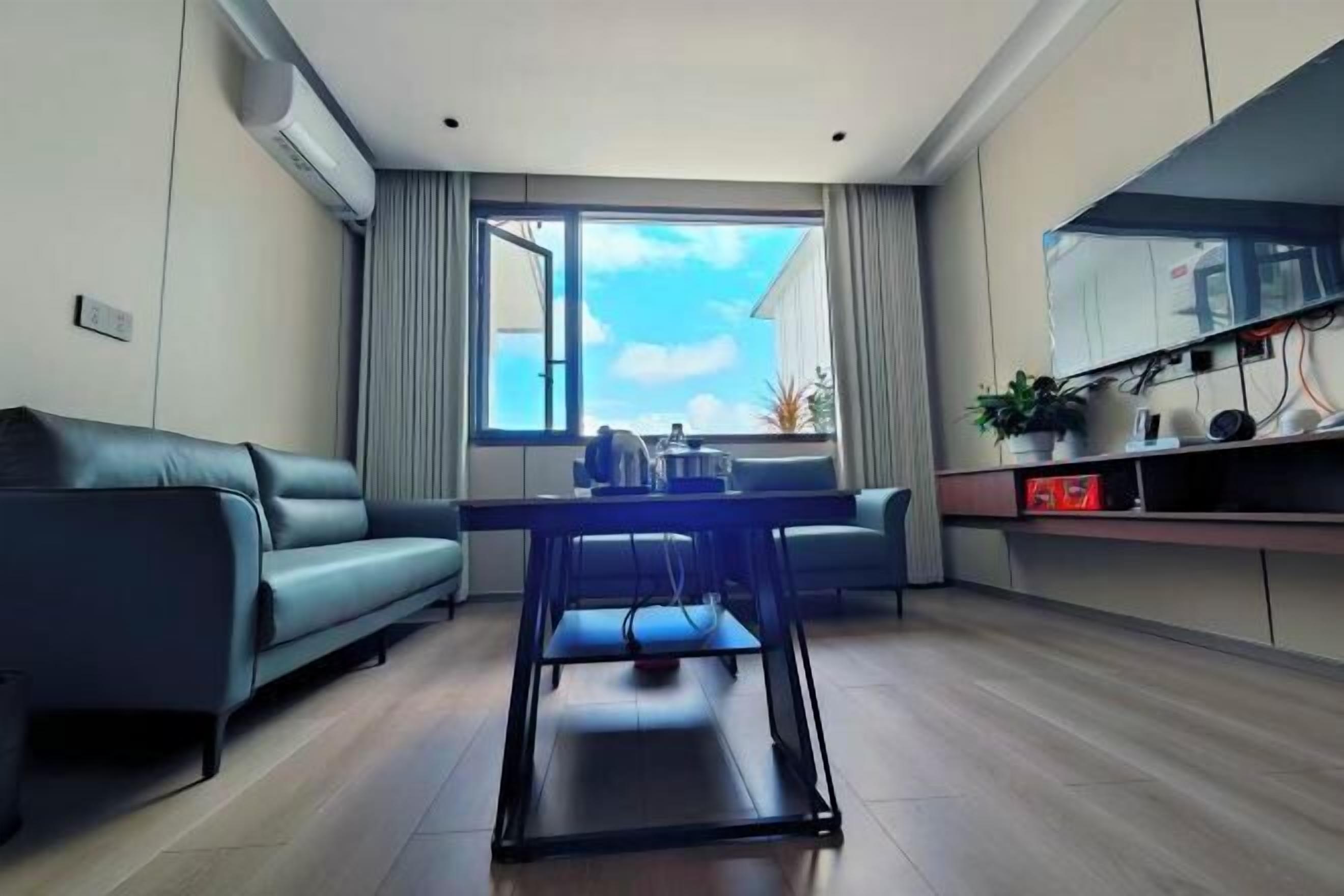Una sala moderna con un sofá, una mesa de comedor, un televisor montado en la pared y un gran ventanal con cortinas.