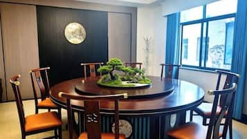 A round dining table with six wooden chairs, a bonsai tree centerpiece, and a wall-mounted clock.