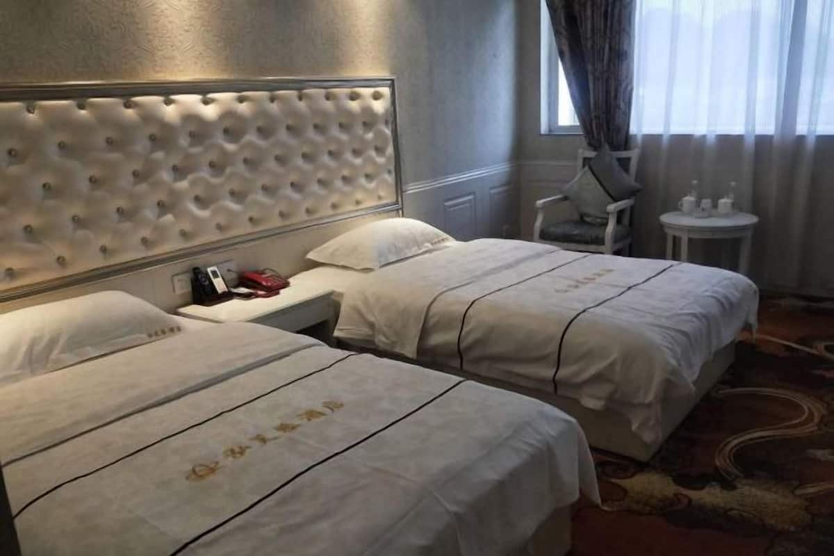 Ein Hotelzimmer mit zwei Betten, einem Kopfteil, einem Sessel, einem kleinen Tisch und einem Fenster mit Vorhängen.