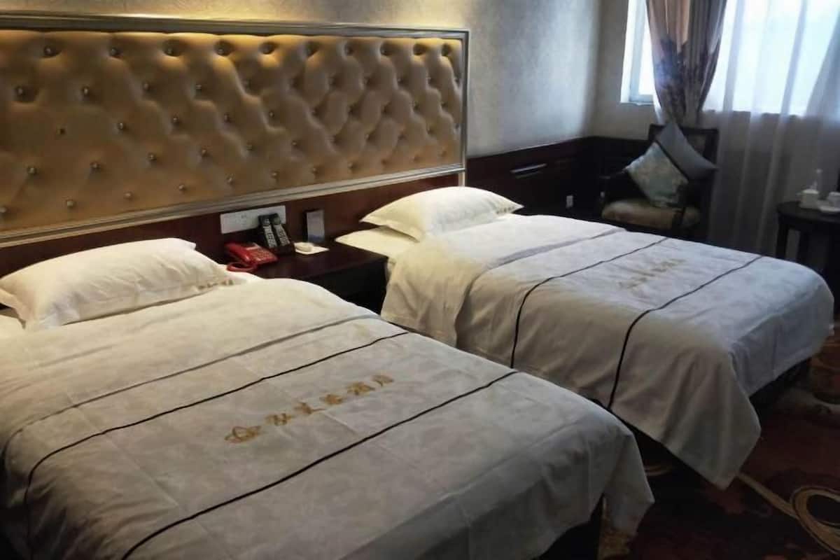 Ein Hotelzimmer mit zwei Betten, einem gesteppten Kopfteil, einem Nachttisch mit Telefon und einem Fenster mit Vorhängen.