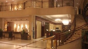 Un vestíbulo de hotel con una escalera de mármol, una mesa de recepción y un candelabro.