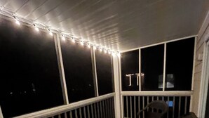 Ein überdachter Außenbereich mit Tisch, Stühlen, Lichterketten und großen Fenstern.