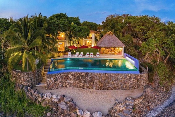 Relax by the infinity pool surrounded by lush greenery and palm trees.