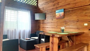 Un interior de madera con muebles de mimbre, un televisor montado en la pared y una pequeña mesa con una planta.
