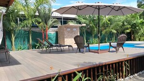 Una terraza de madera con piscina, rodeada de palmeras y sillas.
