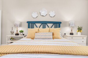 A neatly made bed with a blue headboard, white nightstands with lamps, and decorative wall art. - Top Floor Corner | Two Pools | Private Beach (Santa Rosa Beach)