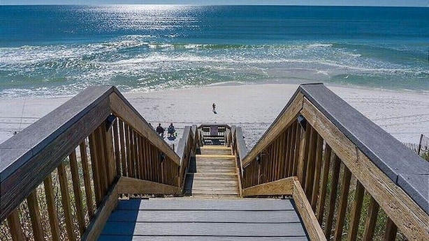 Une promenade en bois qui mène à une plage d’où l’on a une vue dégagée sur l’océan.