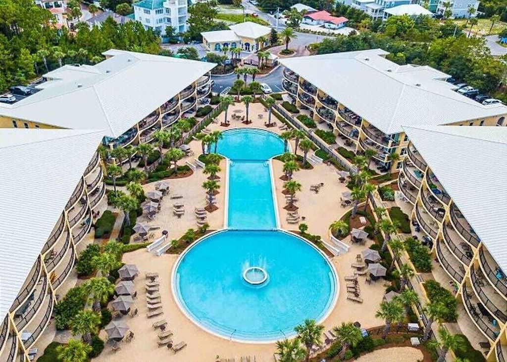 A hotel with a central swimming pool surrounded by lounge chairs and umbrellas, with multiple balconies around the pool.