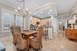 A modern kitchen with white cabinets, a stainless steel refrigerator, and a dining area with wicker chairs and a wooden table. - Top Floor Corner | Two Pools | Private Beach (Santa Rosa Beach)