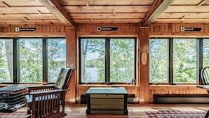 En stuga med träpanel på insidan, stora fönster, en bänk, ett bord och en förvaringskista.