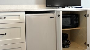 Cocina compacta equipada con refrigerador, microondas y cafetera. Un televisor está montado sobre la encimera.