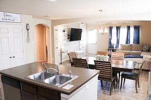 A modern kitchen with a central island and double sink, connected to a dining area with wooden chairs and a table.