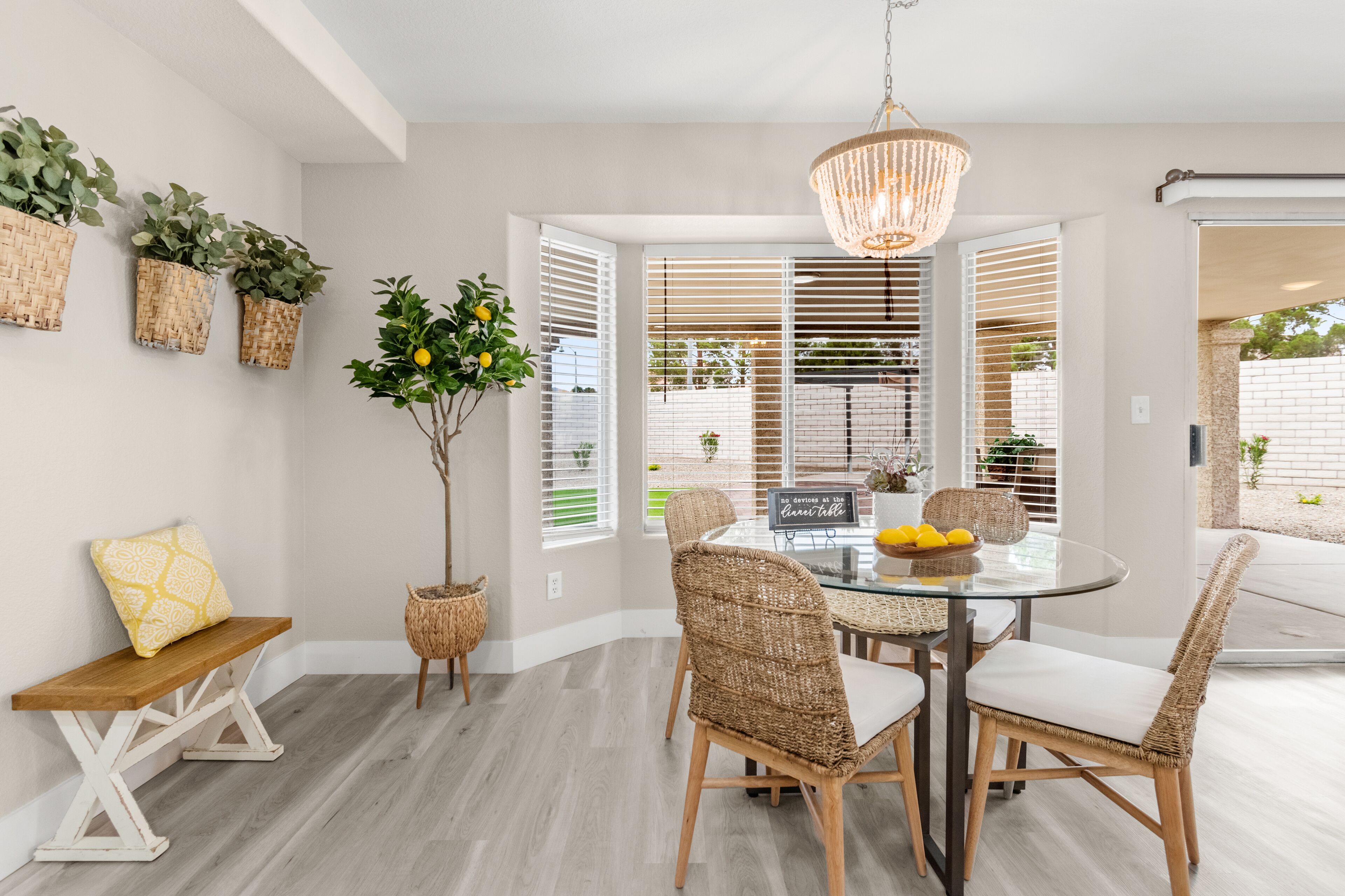 A dining area with wicker chairs, a glass table, and a hanging chandelier.