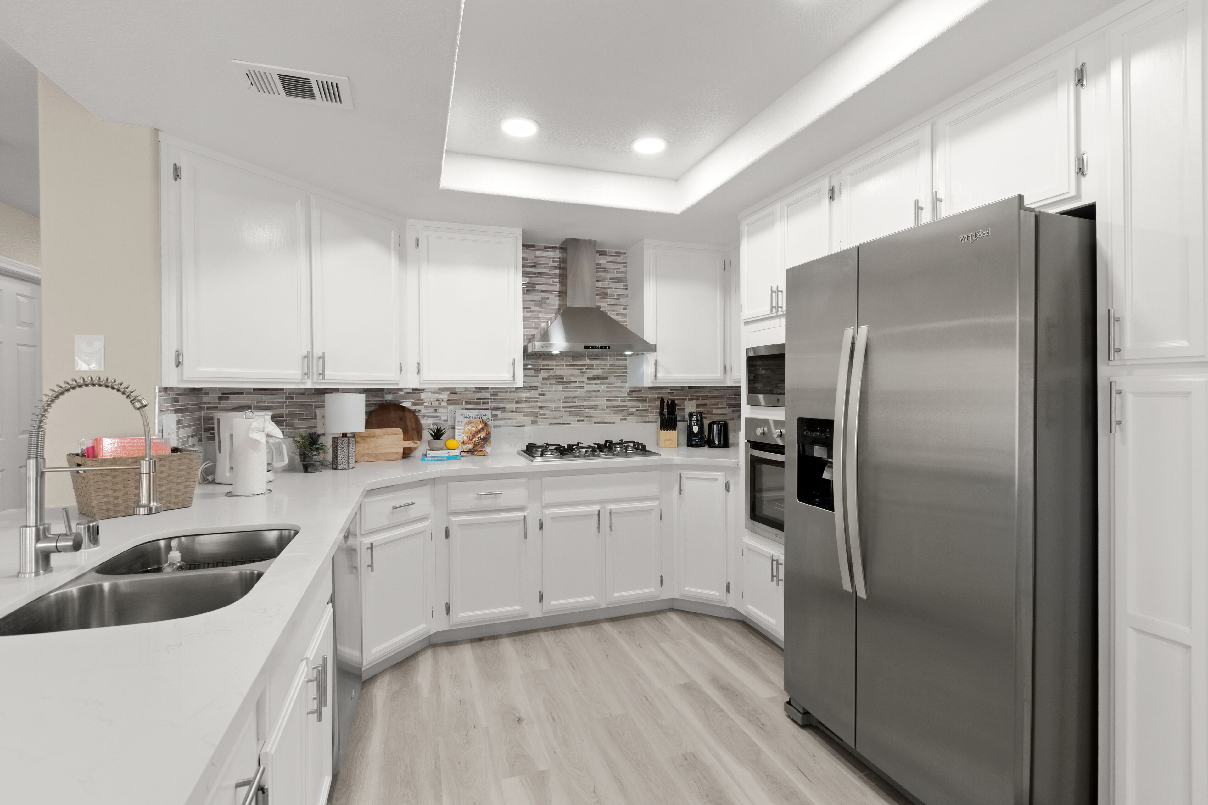 A modern kitchen with white cabinets, a stainless steel refrigerator, a gas stove, and a built-in oven.