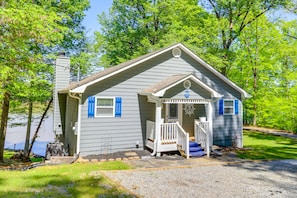 Cozy cabin with a gabled roof and front porch, surrounded by a serene lawn and trees.