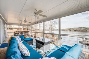 Relax in this serene room with a large window overlooking a tranquil body of water, featuring a comfortable sofa and a wooden deck.