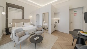 Ett modernt hotellrum med en säng, två fåtöljer, ett litet bord, en spegel och ett litet pentry.