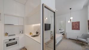 Moderni keittiö, jossa on integroidut kodinkoneet, ruokailutila pöydän ja tuolien kera sekä olohuone, jossa on sohva ja televisio.