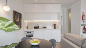 A modern kitchen with white cabinets, a dining table with a bowl of fruit, and a grey sofa.