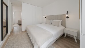 A bedroom with a large bed, bedside tables, a mirror, and a door leading to another room.