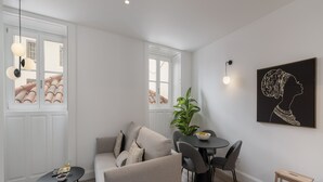 A modern living room with a sofa, a dining table with chairs, a small side table, and a potted plant.