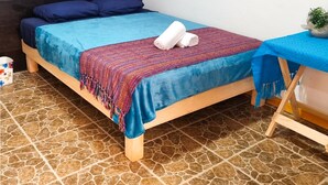 Une chambre à coucher avec un lit, une tête de lit, une décoration murale, une petite table avec une plante et un sol carrelé.