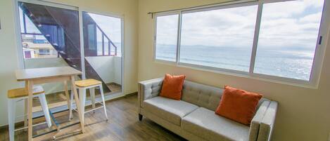 A living room with a sofa, two chairs, a table, and a large window overlooking the ocean.