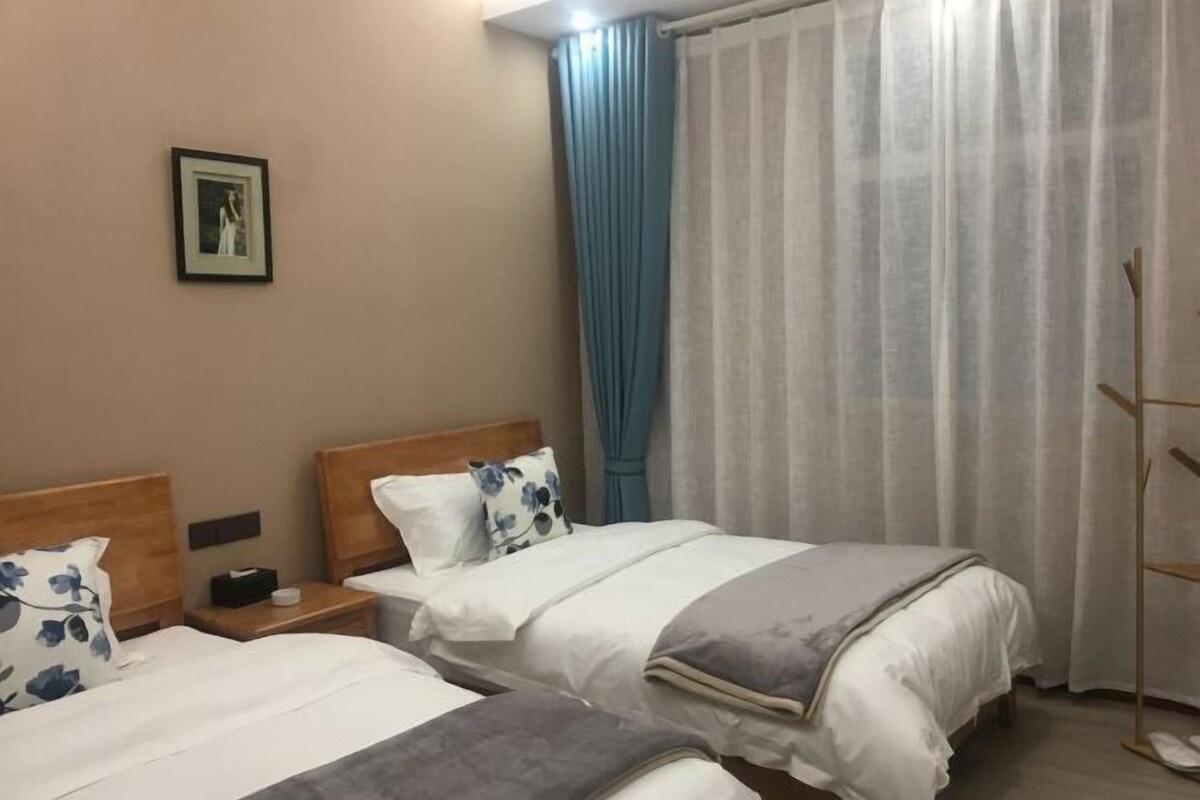 Une chambre d’hôtel avec deux lits, une table de chevet, un tableau au mur et une fenêtre avec des rideaux.