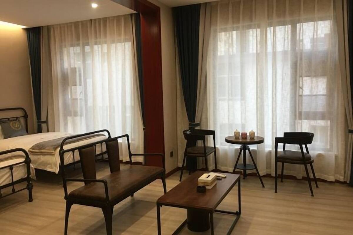 A hotel room with a bed, two chairs, a small table, and a window with curtains.