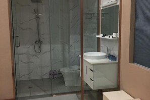 Un baño con cabina de ducha de vidrio, inodoro y lavamanos con espejo.