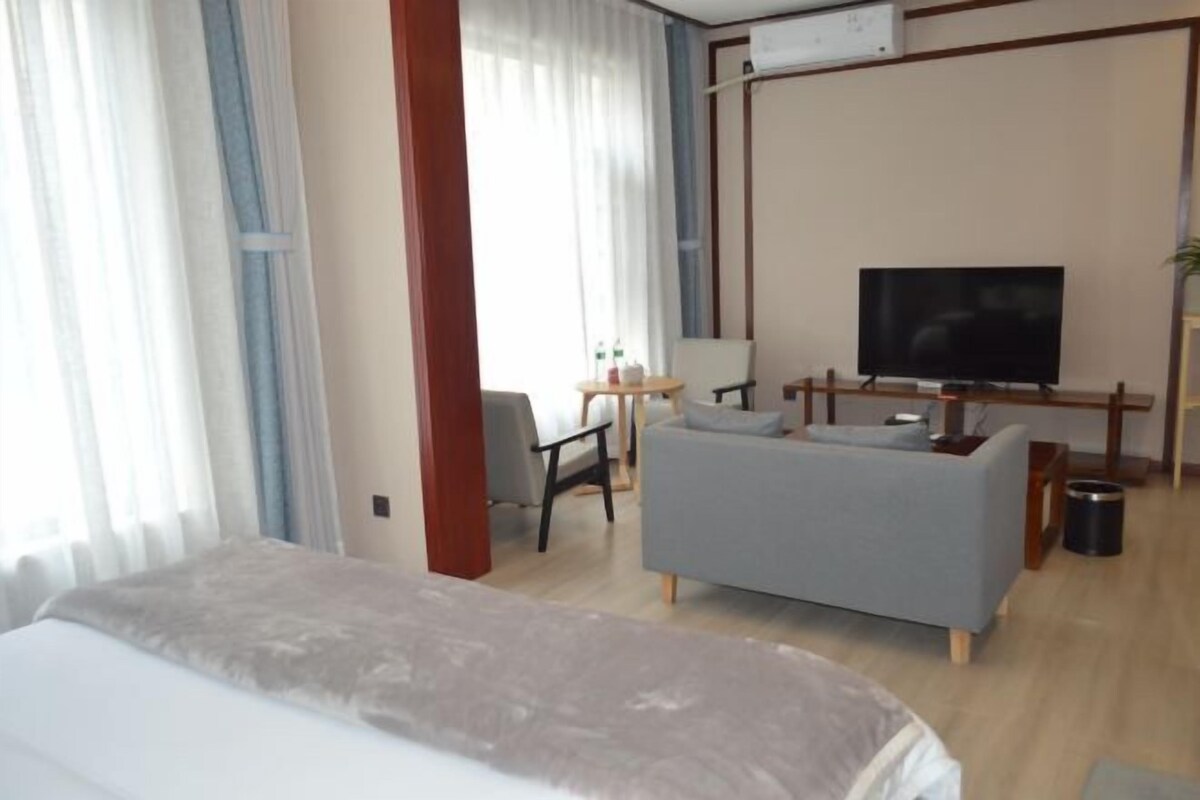 A hotel room with a bed, a grey sofa, a TV, and a small table with a lamp.