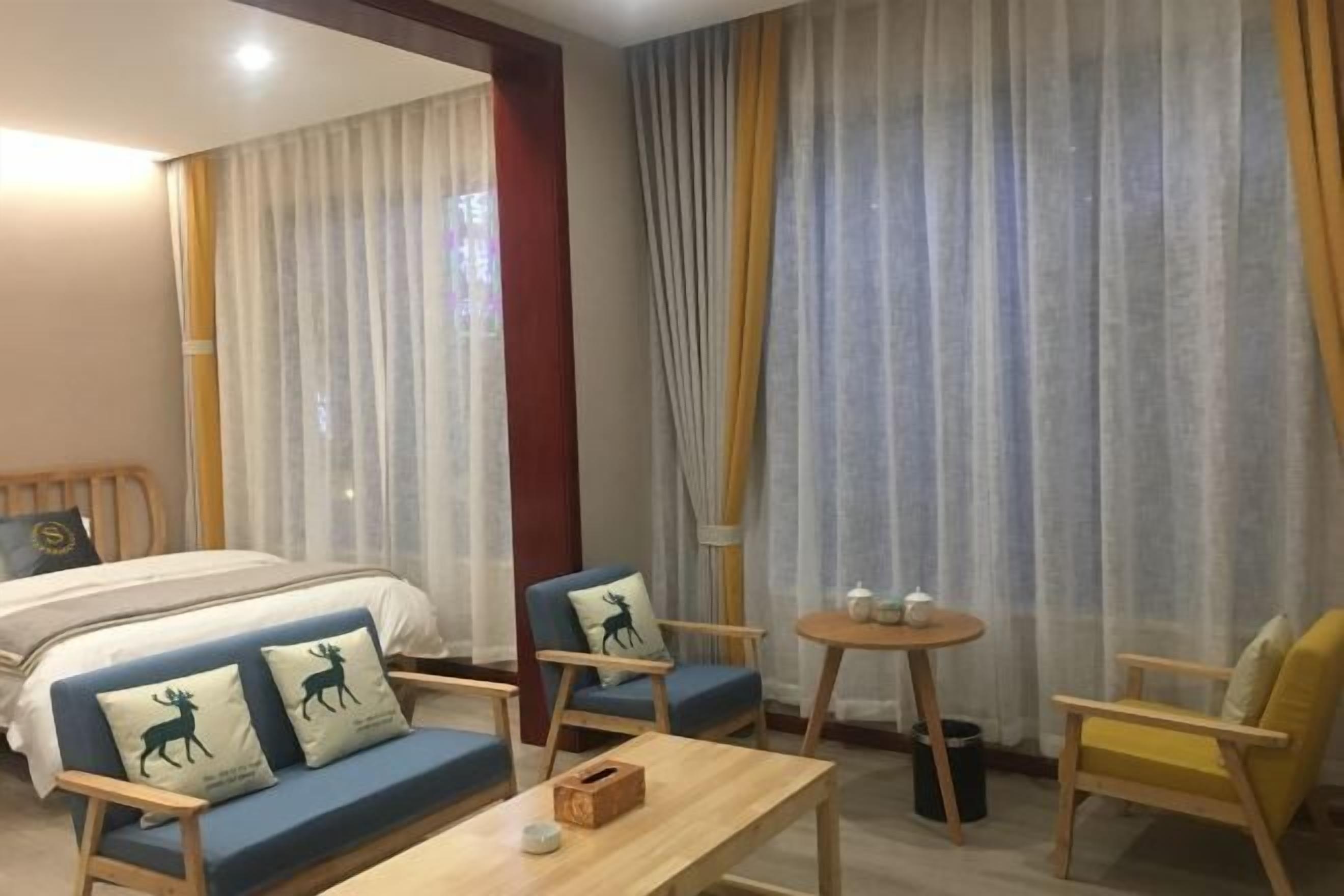 Una habitación de hotel con una cama, dos sofás, una mesita y cortinas.